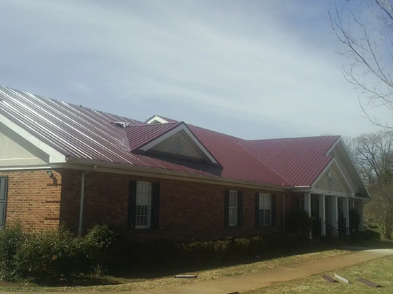 Red metal roof with gabled entries on a long brick building, from a Hail Damage Roof Repair job in Wabasso