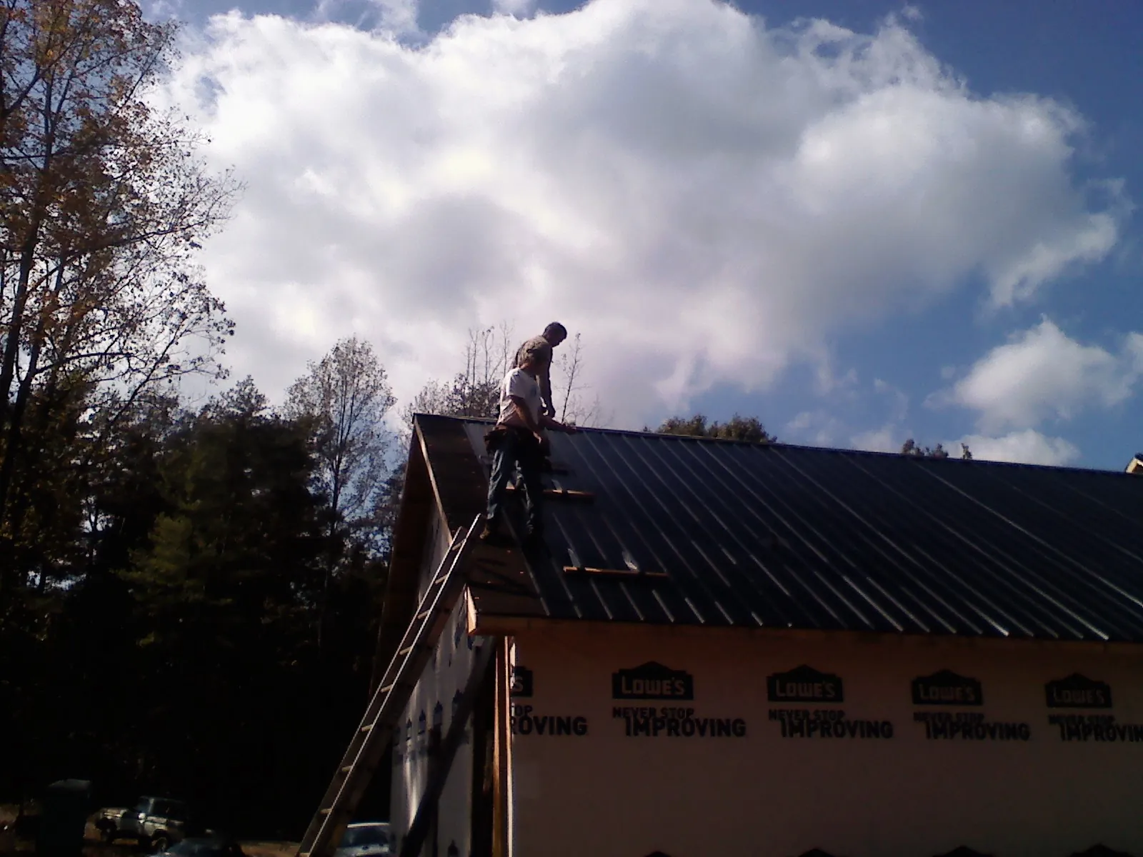 Roofer fastening dark metal panels high against a cloudy sky, from a Roof Inspection job in Wabasso