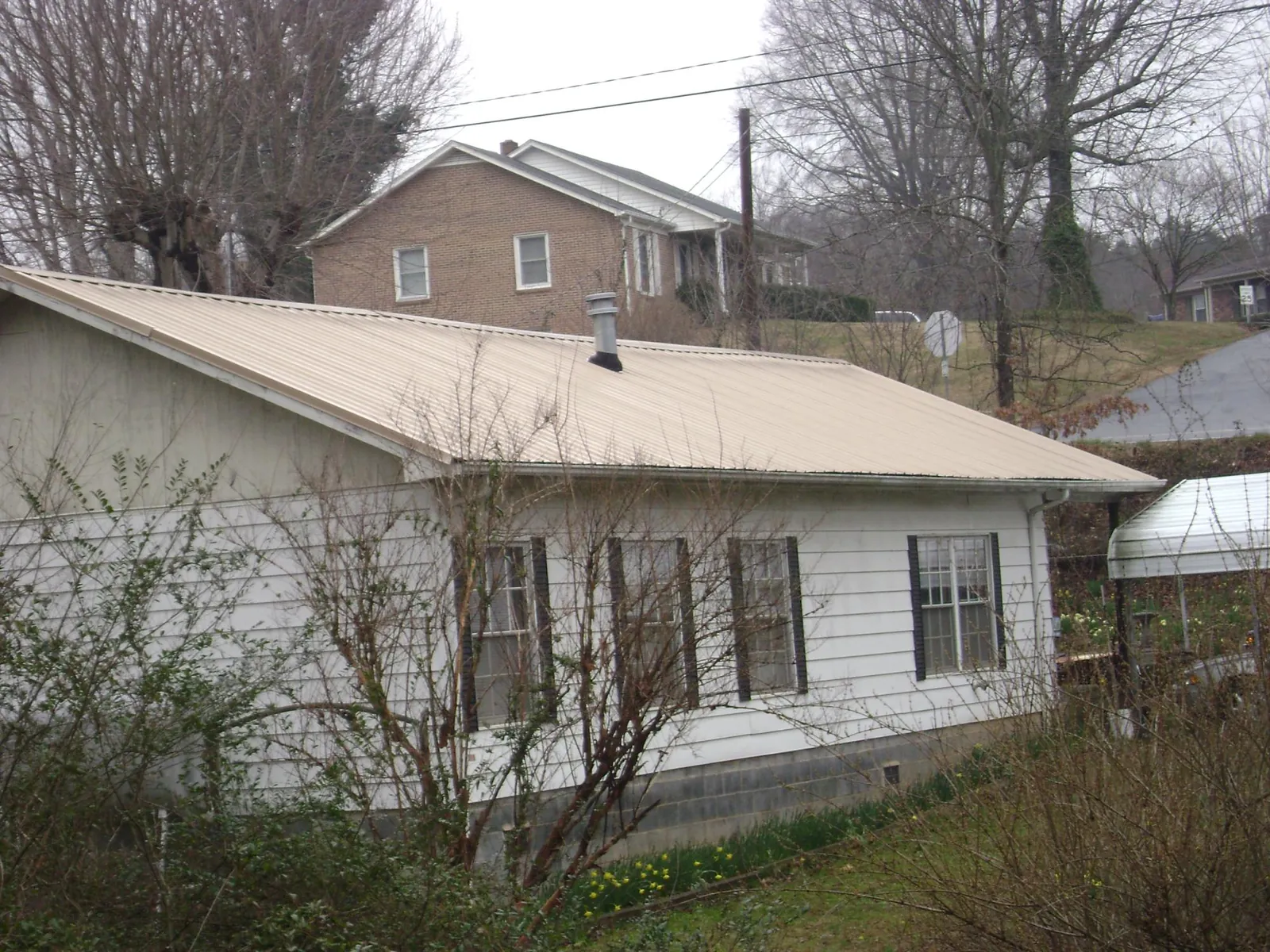 Tan metal roof on a white sided house set into a hillside — Commercial Roofing by Roofing Brothers in Wabasso